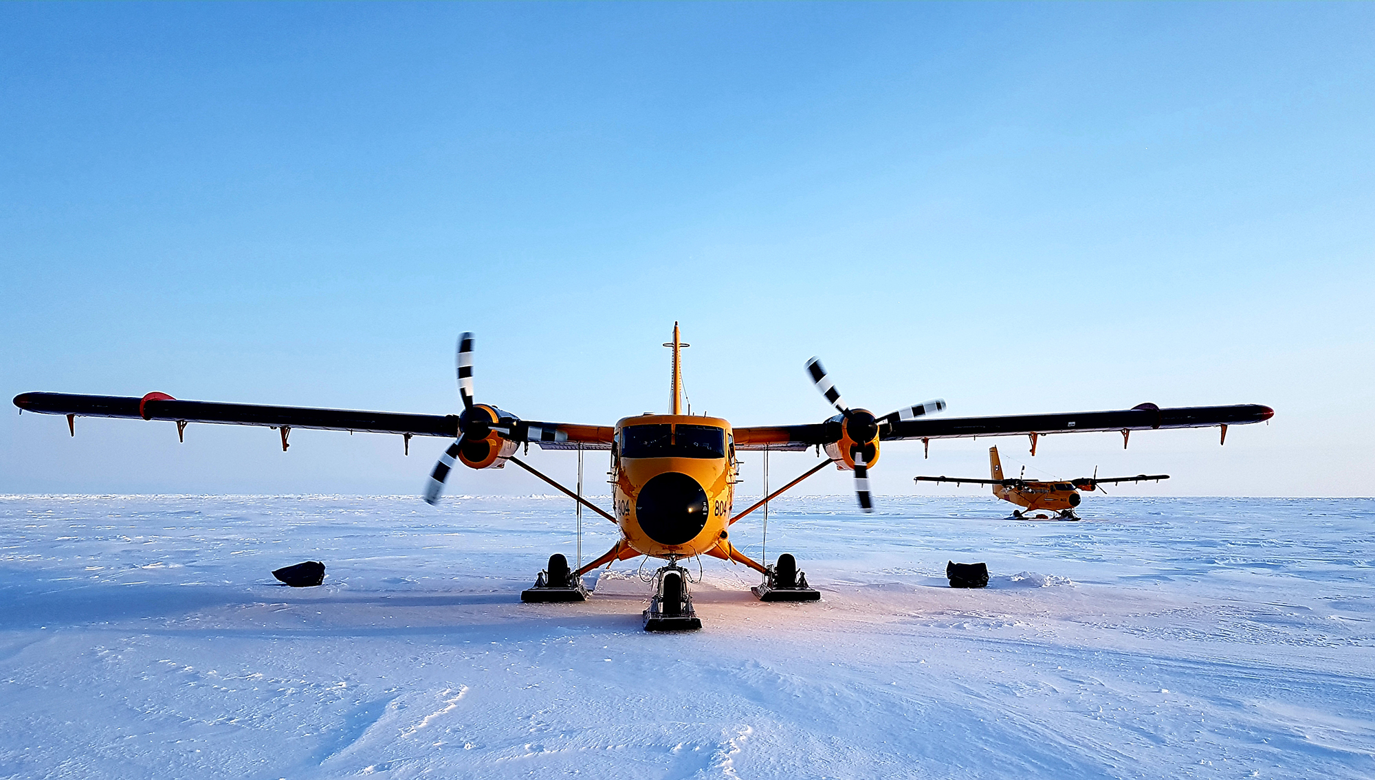 Two orange twin-propeller aircraft equipped with skis on snow in the Arctic.